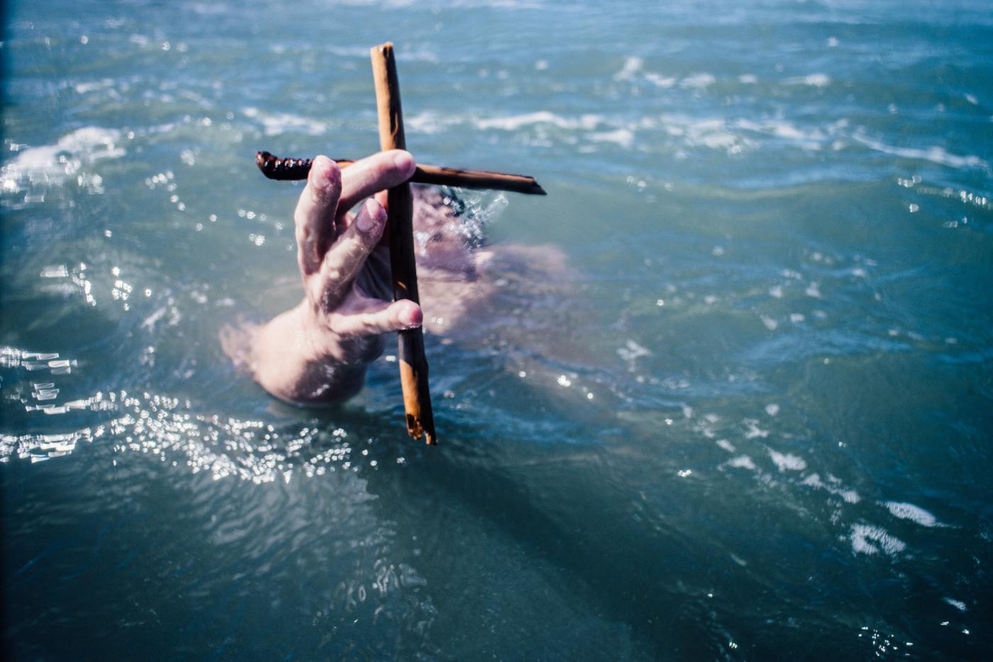 Ocean water with two clasping hands clutching a cross